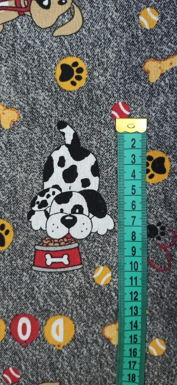 Loneta Perritos y Huesos fondo gris jaspeado con cinta métrica para apreciar la escala del estampado
