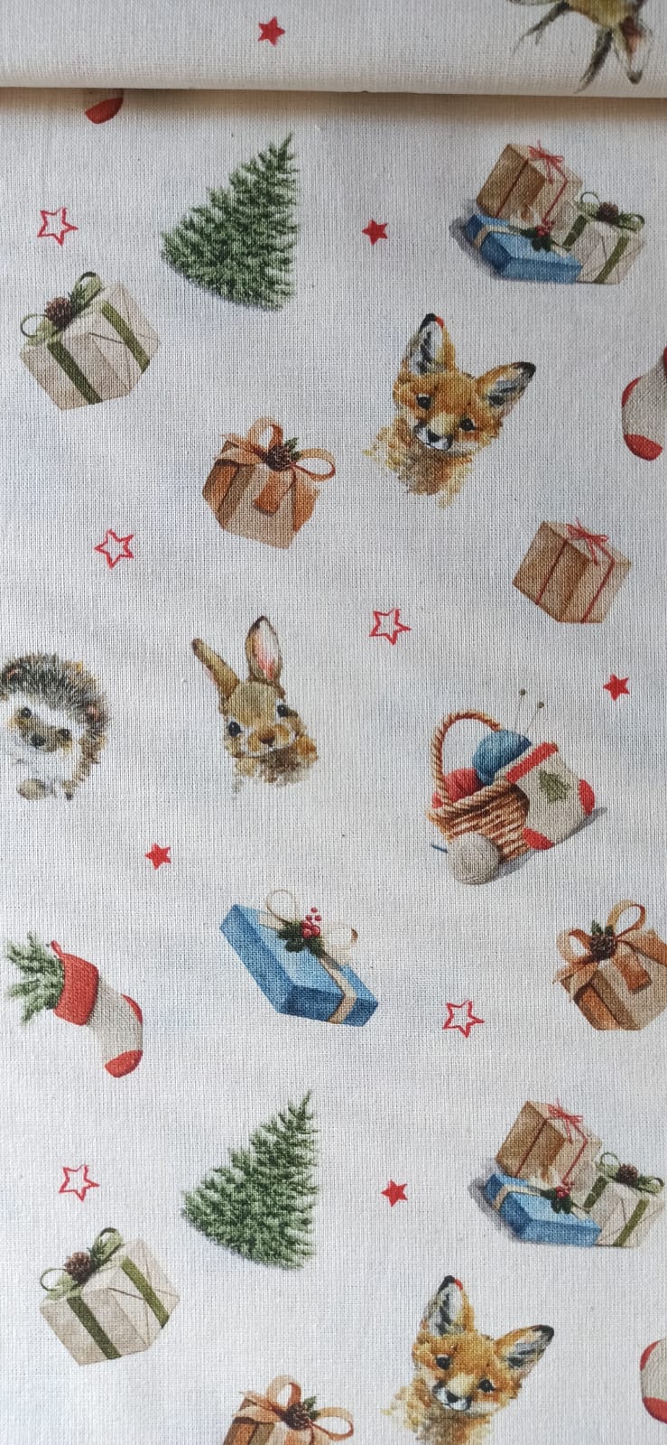 Detalle de zorro, conejo y erizo entre regalos y abetos en el estampado navideño de algodón.