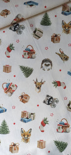 Tela de algodón sobre fondo claro con animales del bosque, regalos, abetos y estrellas rojas de Navidad.