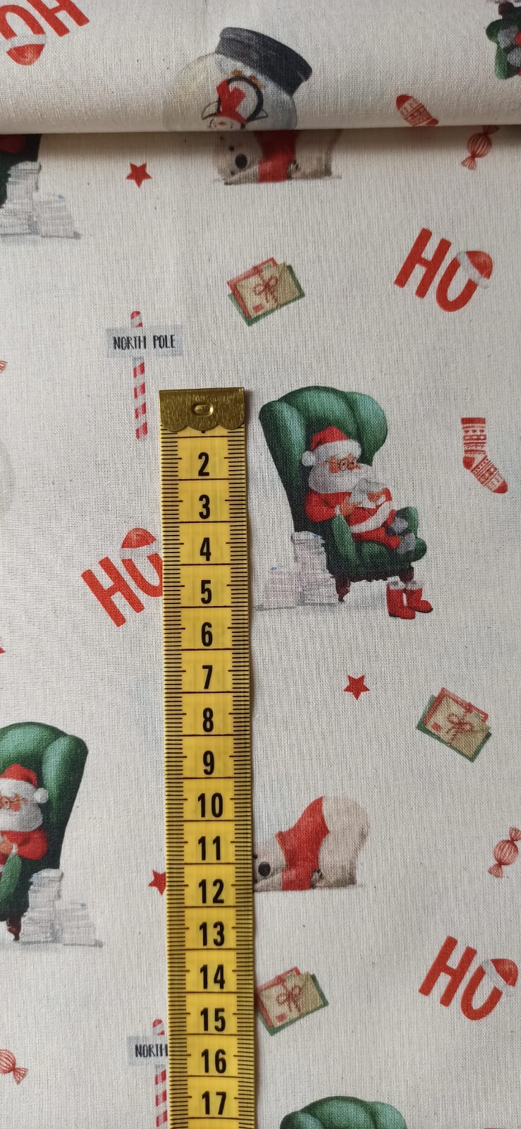 Detalle de Papá Noel en sillón verde junto a una cinta métrica para apreciar el tamaño del estampado.