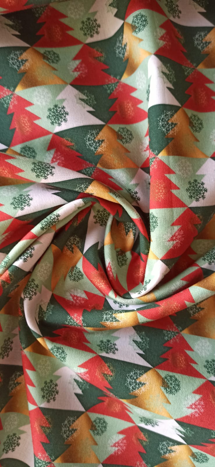 Tela de algodón con pinos y copos multicolor dispuesta en espiral para mostrar el estampado navideño.